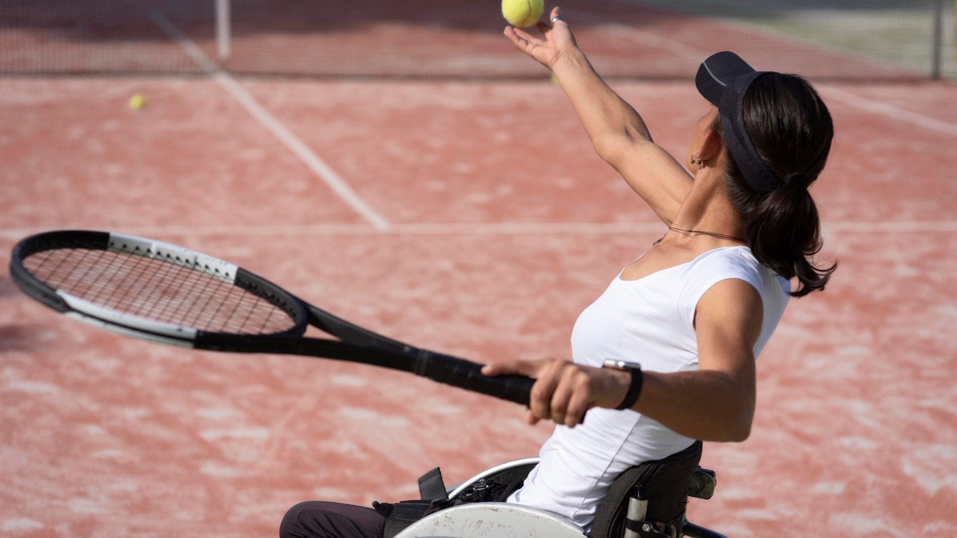woman in a wheelchair serving a tennis ball showing the Paralympics codes