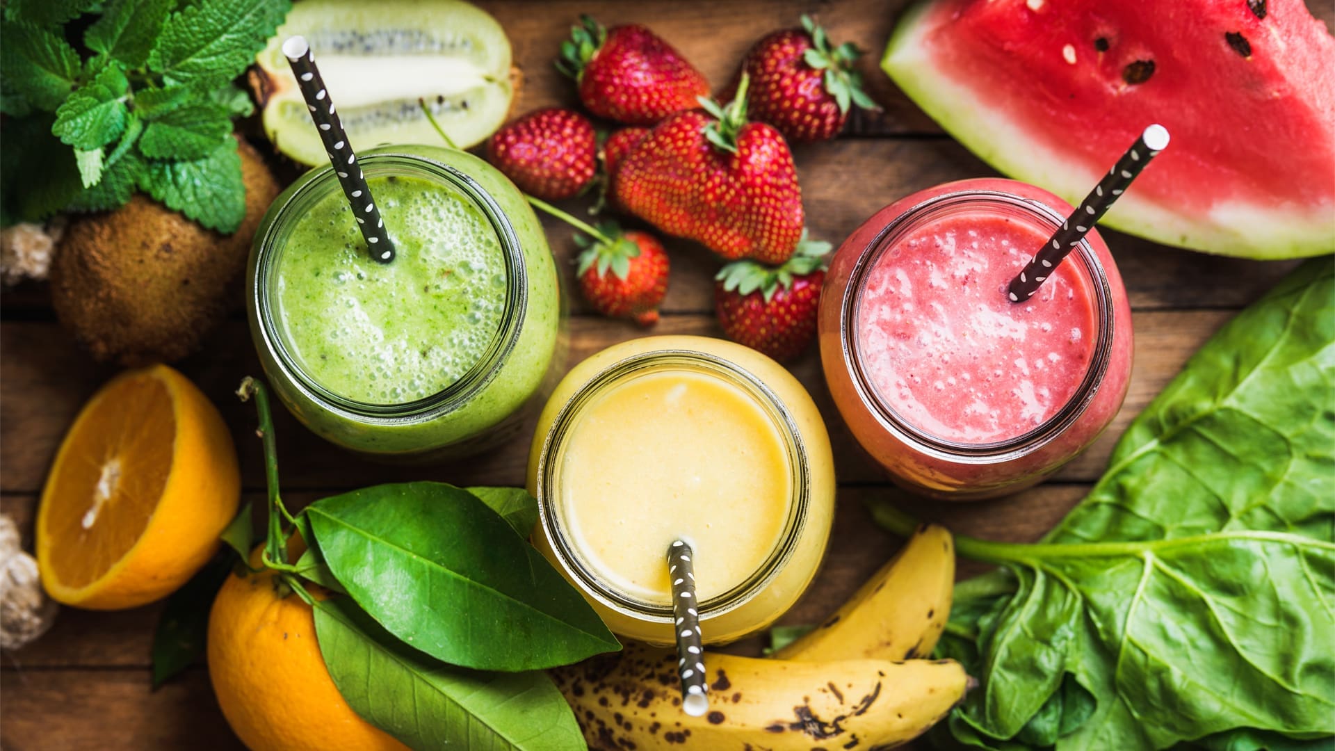 Freshly blended fruit smoothie recipes for weight loss of various colors and tastes in glass jars in rustic wooden tray.
