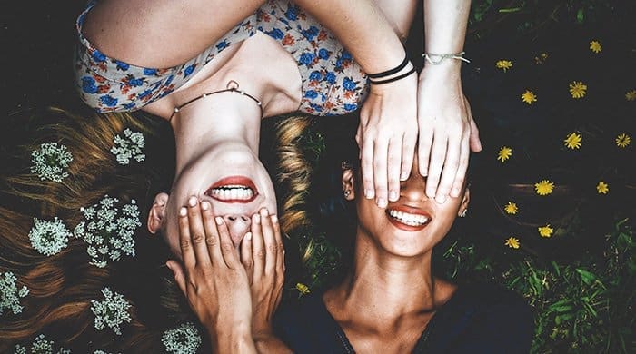 To women lying in a field with their hands over their eyes to represent falling in love with a woman