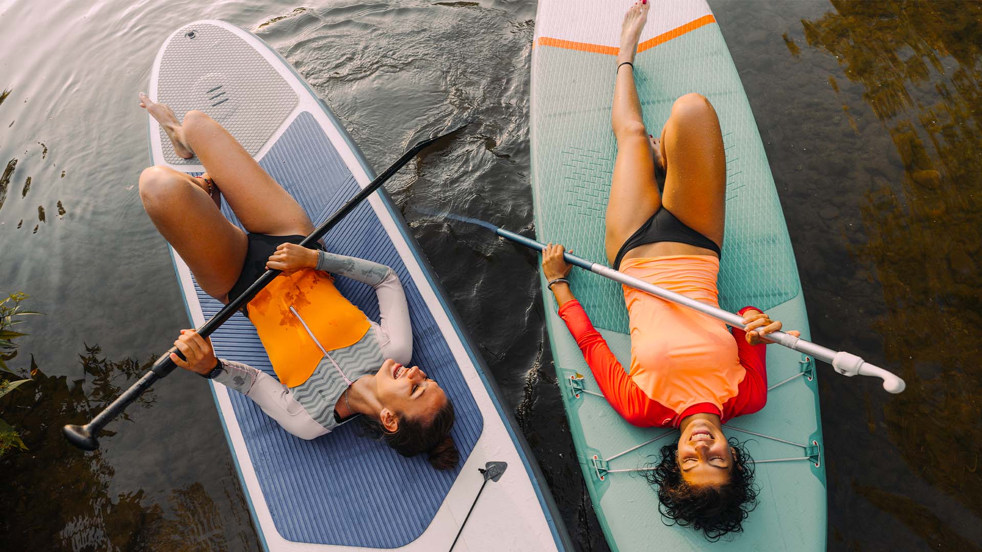Two woman laughing on paddle boards in the ocean.