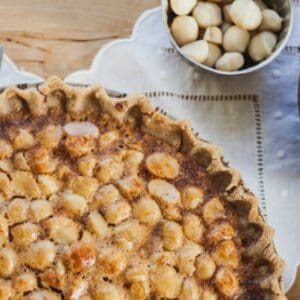 macadamia nut pie with knife balancing on top, a fork in a bowl and macadamia nuts in a bowl
