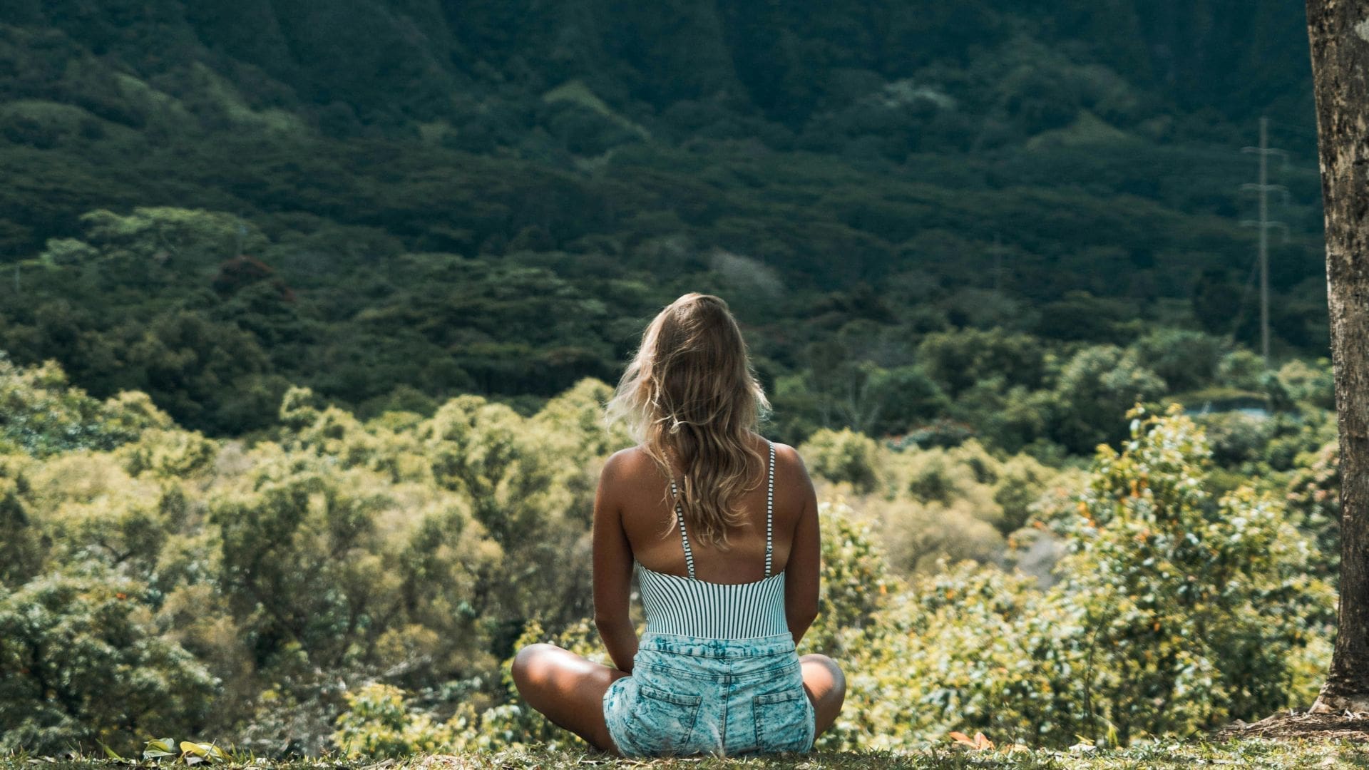 woman sitting in nature surrounded by green trees practise mindfulness