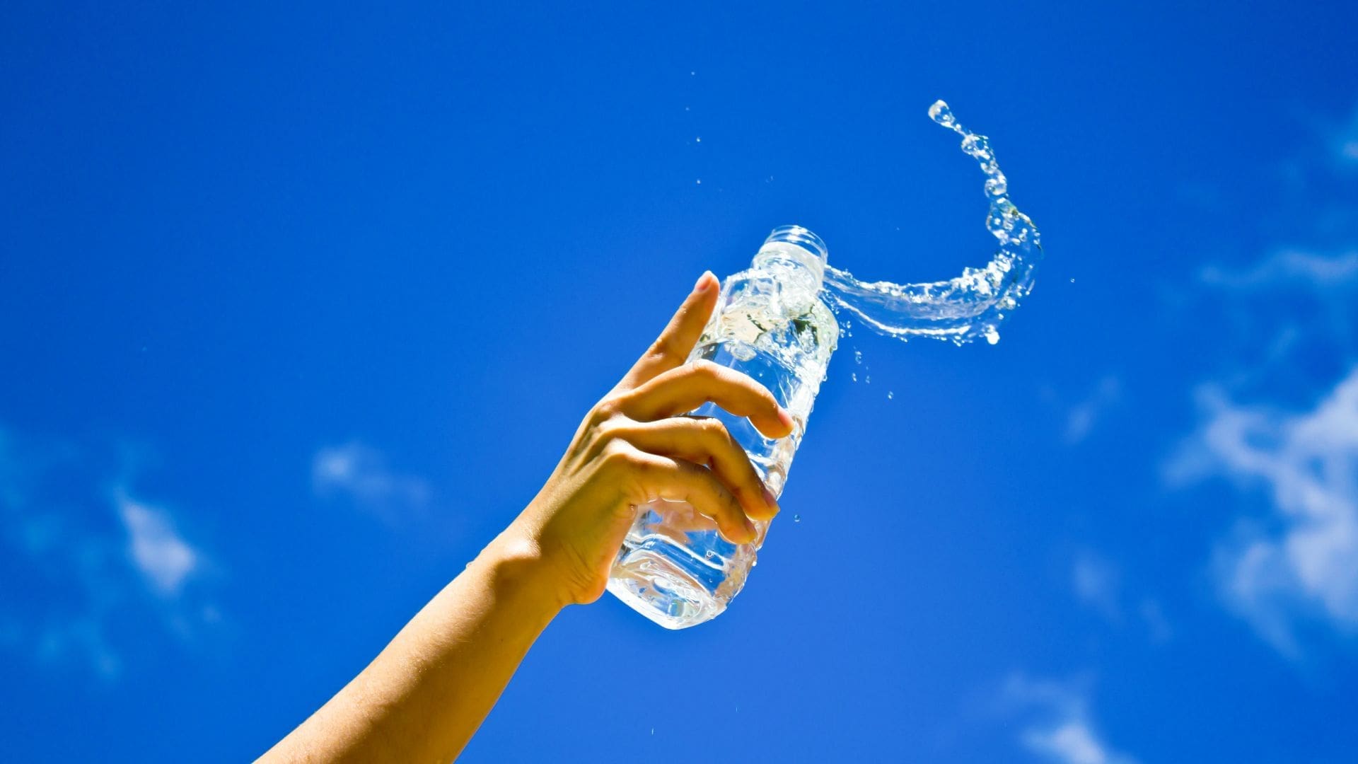 spilling water bottle against bright blue sky to conceptualise a leaky bladder during workouts or urinary incontinence